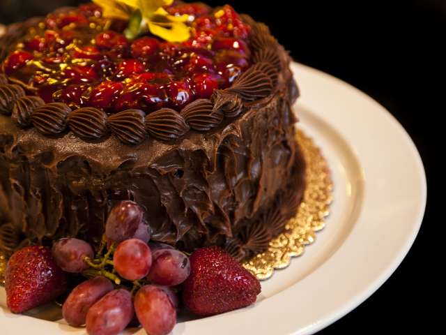 Торт с шоколадным кремом, виноградом и клубникой на белой тарелке