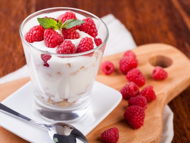 Десерт с йогуртом и свежей малиной в стеклянном стакане на столе