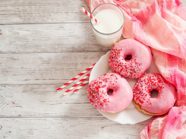 Три аппетитных пончика с розовой сахарной слазурью и стаканом молока