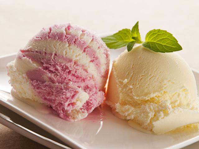 Два шарика фруктового мороженого с листьями мяты на белой тарелке