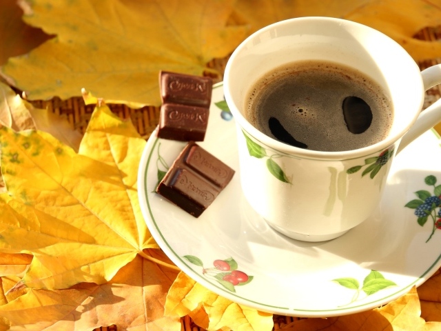 Чашка кофе с черным шоколадом на столе с желтыми листьями