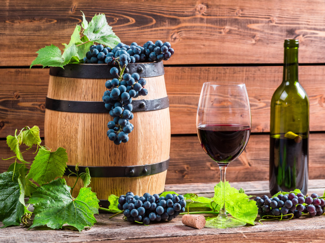 Бокал вина с бочкой и бутылкой на столе с гроздьями синего винограда с листьями