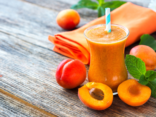 Абрикосовый смузи в стакане на столе со свежими ягодами