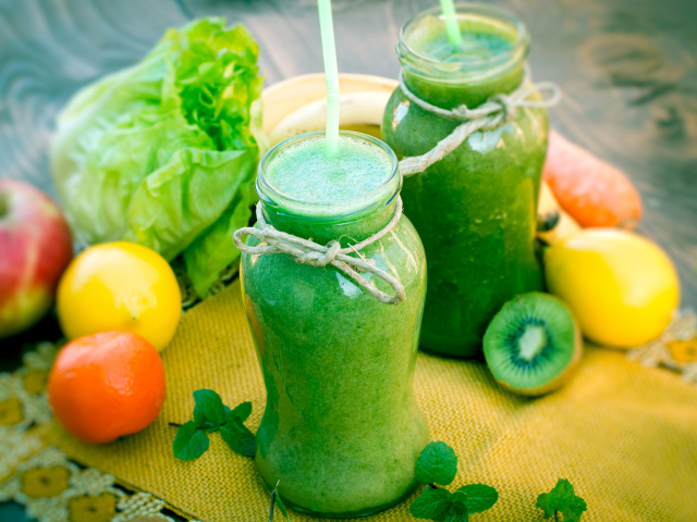 Зеленый смузи в бутылках с трубочками и фруктами на столе