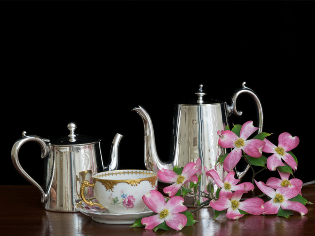 Чайники с чашкой с цветами на столе на черном фоне