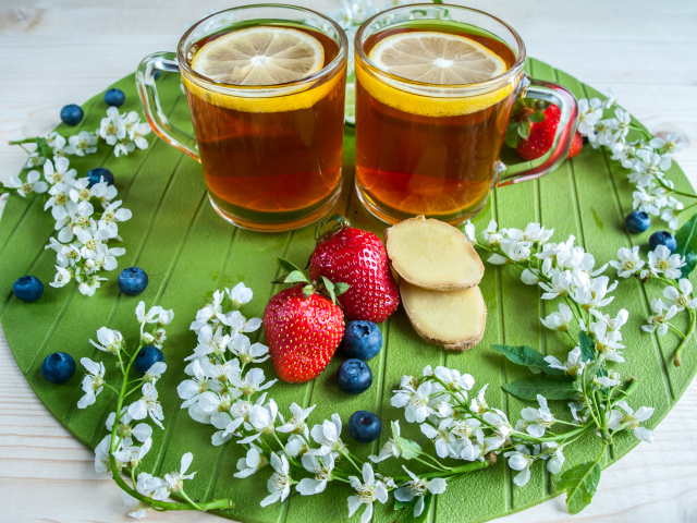 Две чашки чая с лимоном на столе с ягодами клубники, черники и кусочками имбиря