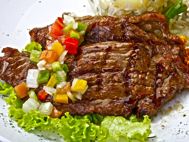 Кусок сочного жареного мяса с овощами и листьями салата