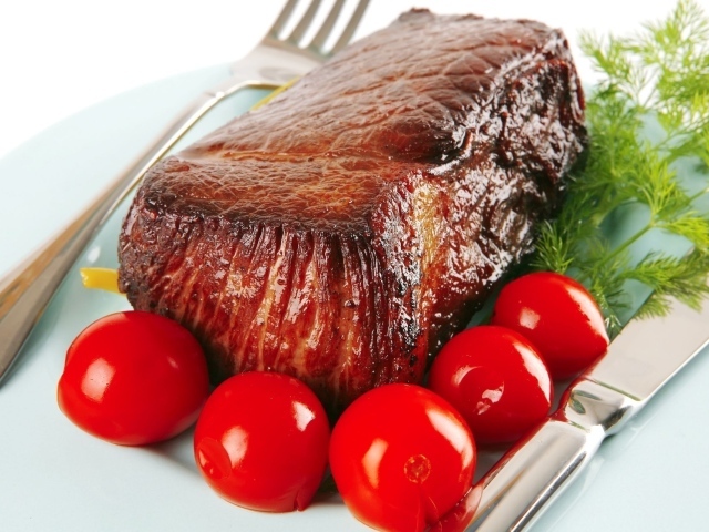 Кусок мяса с маринованными помидорами и зеленью на блюде