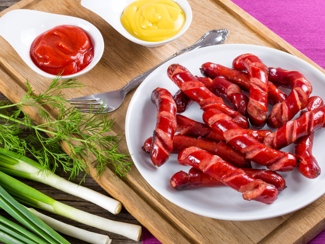 Аппетитные сосиски барбекю на столе с соусом и зеленью