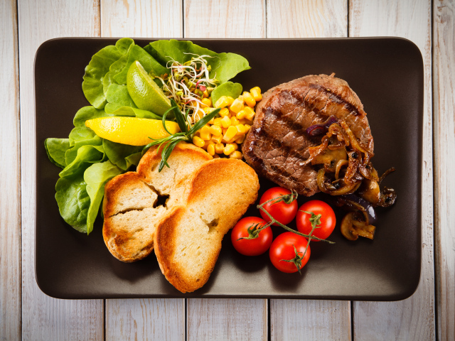 Аппетитный кусок жареного мяса на тарелке с овощами и гренками