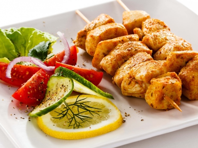 Шашлык из курицы на белой тарелке с овощами и кусочком лимона