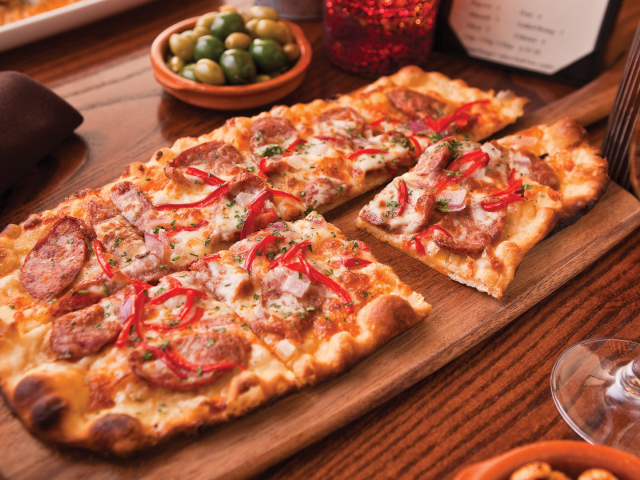 Порезанная на кусочки пицца лежит на разделочной доске