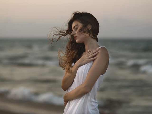 Мечтательная девушка в белом наряде стоит на берегу океана