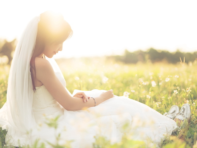 Девушка азиатка в платье невесты сидит на траве в поле 