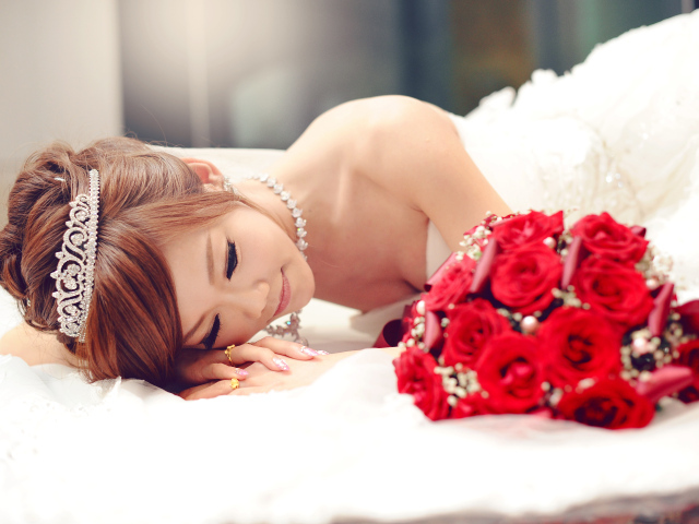 Красивая девушка азиатка в свадебном платье с букетом красных роз