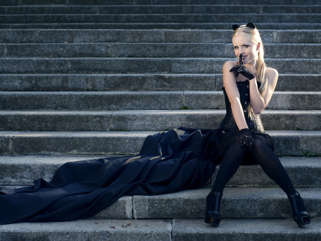 Красивая девушка блондинка  сидит на ступеньках в черном костюме