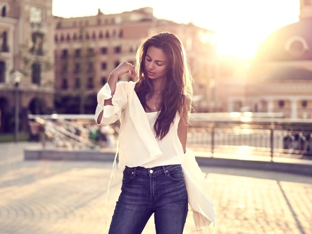 Красивая девушка в синих джинсах стоит на фоне солнца