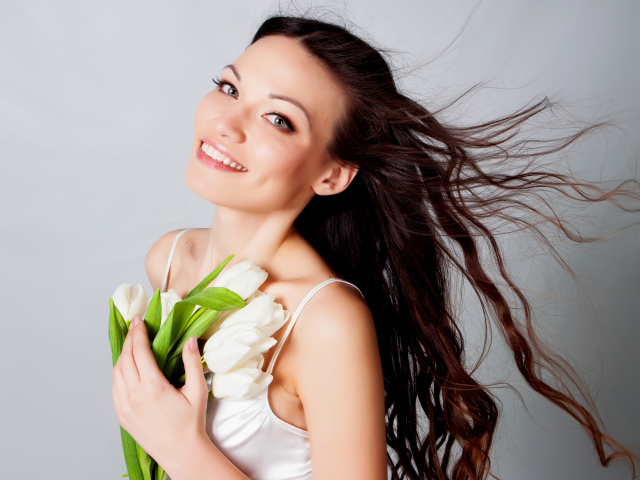 Красивая улыбающаяся брюнетка с букетом тюльпанов на сером фоне