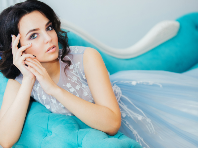 Девушка брюнетка в красивом платье лежит на голубом диване