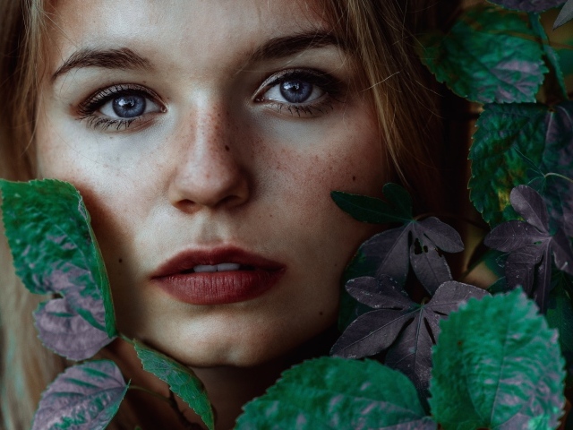 Лицо красивой голубоглазой девушки украшено зелеными листьями