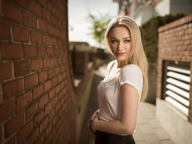 Молодая девушка блондинка у кирпичной стены 
