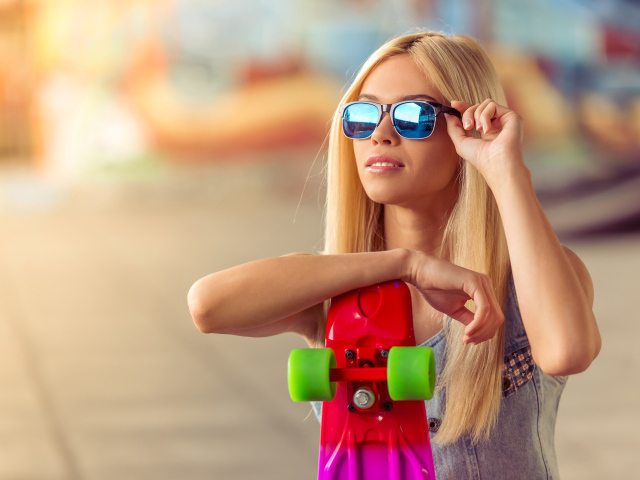 Молодая блондинка в солнечный очках со скейтбордом