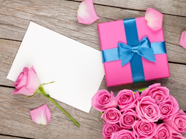 Коробка с подарком на столе с букетом розовых роз и листом бумаги