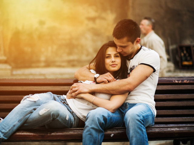 Влюбленная пара сидит на деревянной лавке в парке
