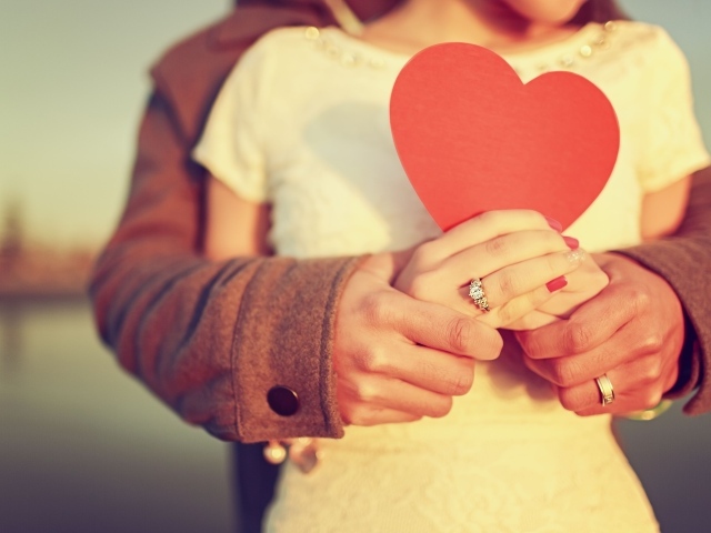 Влюбленная пара держит в руках красное бумажное сердце