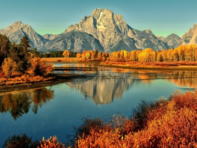 Горы и осенние деревья отражаются в реке 
