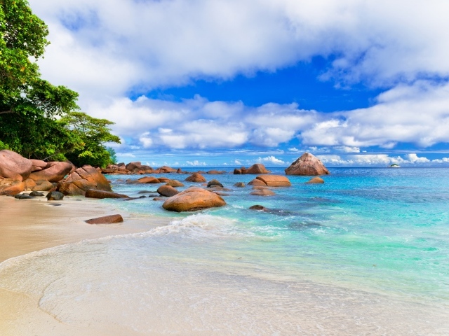 Большие камни на белом песке у голубой воды океана