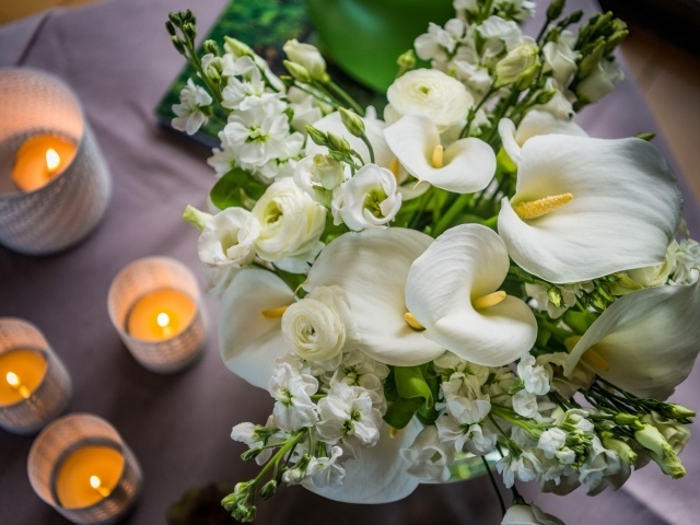 Букет белых цветов зантедеския и левкой с зажженными свечами на столе