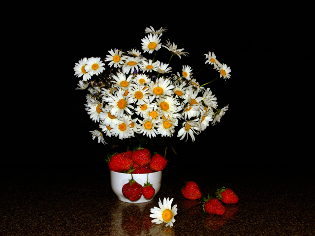 Белые полевые ромашки и клубника на столе на черном фоне