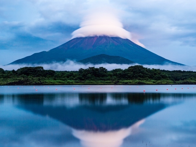 Вулкан Фудзияма в белых облаках отражается в воде озера