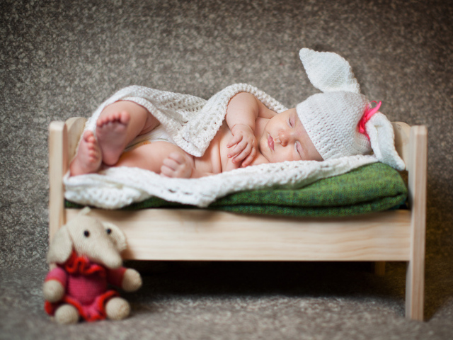 Грудной ребенок спит в деревянной кровати в белом вязаном костюме зайчика