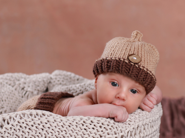 Грудной ребенок лежит в вязаной коричневой шапке