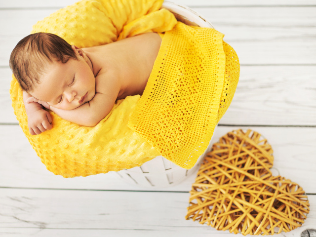 Грудной ребенок спит на желтой подушке с плетеным сердцем