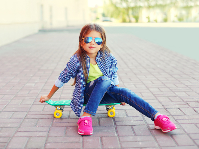Девочка в солнечных очках сидит на скейтборде