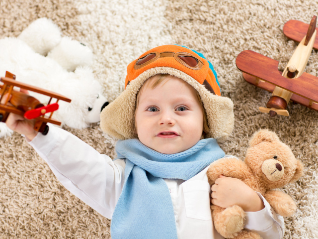 Маленький мальчик в шапке и игрушечным самолетом и медвежонком в руках