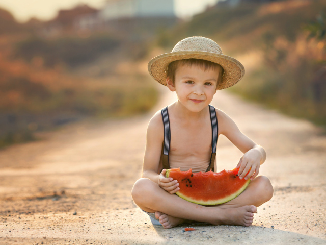 Маленький мальчик в шляпе сидит на дороге с долькой арбуза