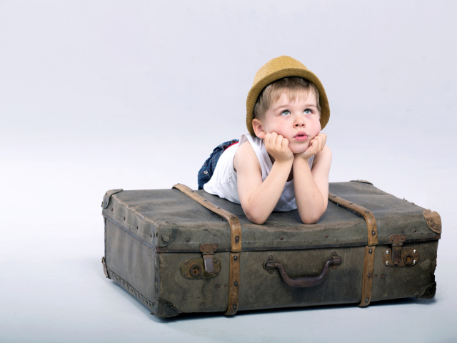 Маленький мальчик лежит на большом чемодане на сером фоне
