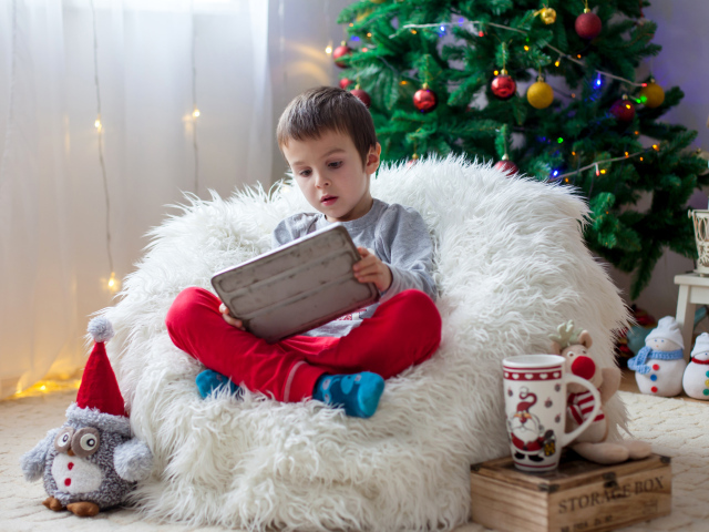 Маленький мальчик сидит в мягком кресле у новогодней елки