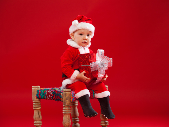 Маленький мальчик сидит на стуле с новогодним подарком
