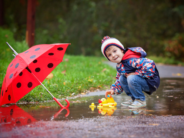 Маленький мальчик пускает резиновую уточку в лужу после дождя