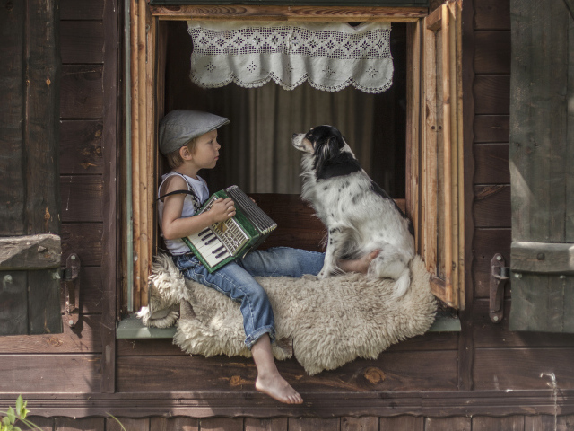Маленький мальчик с гармошкой сидит на подоконнике с собакой