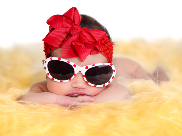 Маленькая забавная малышка в очках и с красным бантом на голове