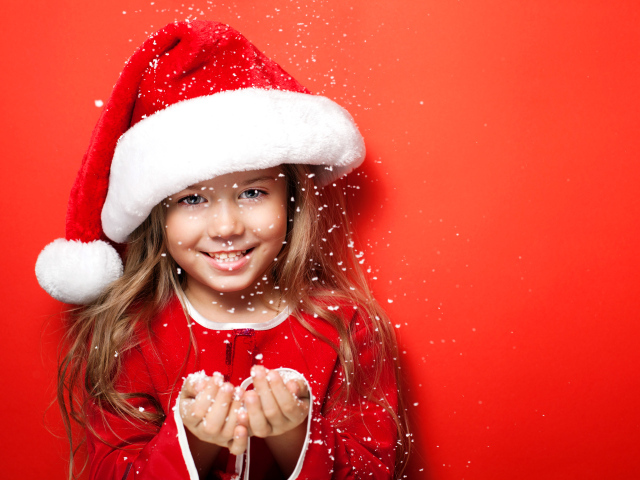 Маленькая девочка в новогодней шапке ловит руками снежинки