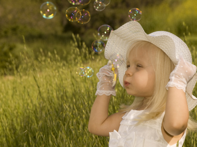 Маленькая девочка в большой белой шляпе пускает мыльные пузыри