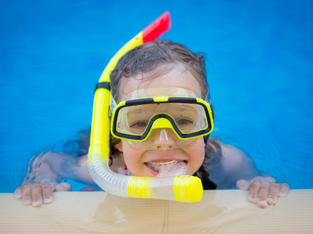 Маленькая девочка в маске с трубкой плавает в бассейне