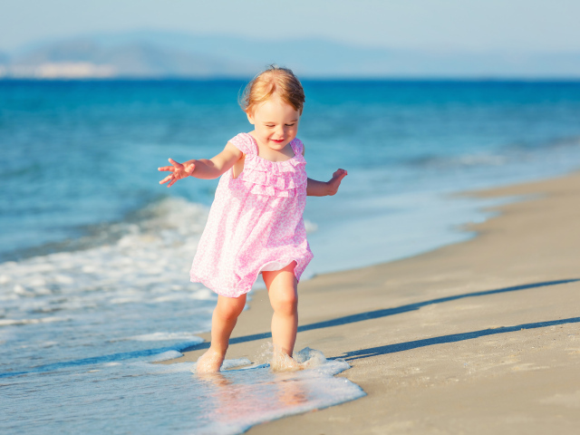 Маленькая девочка в розовом платье гуляет по морскому песку